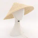 Chapeau chinois en paille jaune et pointu posé sur une tête de mannequin blanc.
