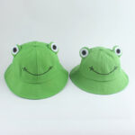 Deux bobs verts avec des yeux de grenouille et un sourire noir cousu dans le tissu