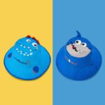 deux chapeaux bleus réversibles, dinosaure et requin, sur fond jaune et bleu