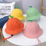Superbes petits chapeaux seau avec une petite queue de pomme sur le dessus. Décliné en vert, orange, jaune, rose et beige. Ils sont posés sur une table près d'un fauteuil.