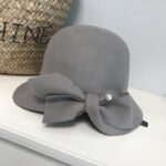 Magnifique chapeau cloche en laine grise, ajustable avec une pice à perle. Il est posé sur une étagère près d'un panier.