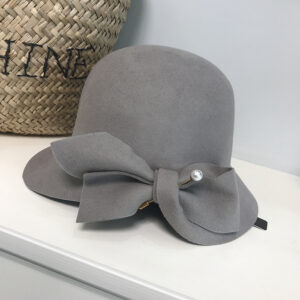 Magnifique chapeau cloche en laine grise, ajustable avec une pice à perle. Il est posé sur une étagère près d'un panier.
