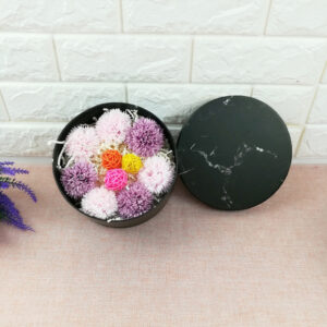 Boîte à chapeau noire marbrée remplie de fleurs de champs pour la présentation et posée contre un mur de parement blanc.