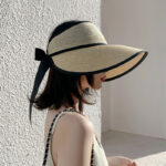 Femme de profil dans une rue portant un débardeur blanc et un chapeau de paille avec un ruban noir.
