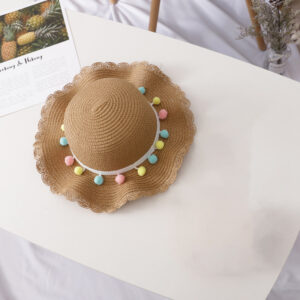chapeau en paille marron pour fille avec pompons colorés, sur une table blanche