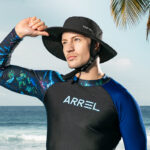 homme en combinaison de surf portant un chapeau de surf noir, à la plage
