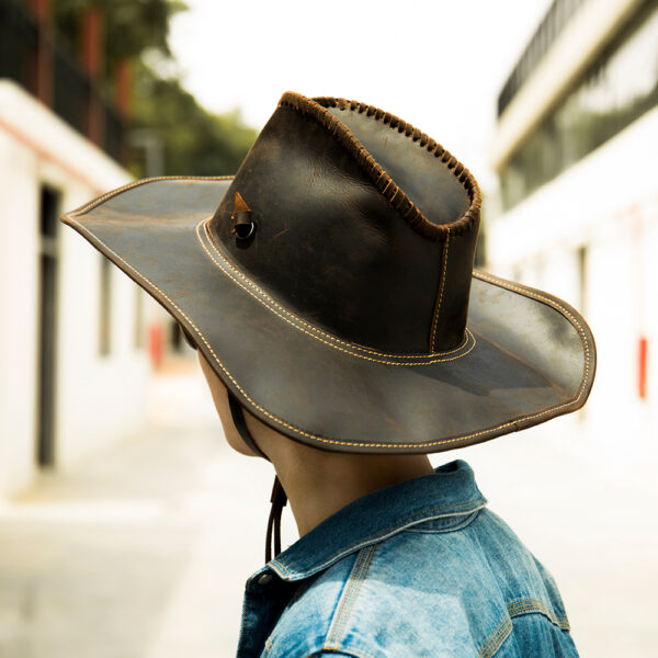 Homme de dos dans une rue lumineuse portant une veste en jean et un chapeau australien en cuir noir.