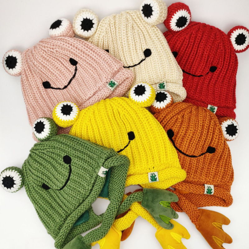 Chapeau de couleurs rose, blanc, rouge, vert, jaune et orange les uns sur les autres avec des yeux de grenouilles et un sourire noir sur chaque chapeau.
