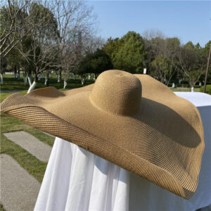 Chapeau capeline, à larges bords, en paille, beige, posé sur une table avec une nappe blanche en exterieur