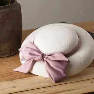 Chapeau plat de mariage blanc, entouré par un ruban avec nœud violet, posé sur une table en bois