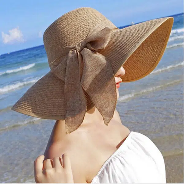 Chapeau en paille de couleur beige, entouré par un ruban avec nœud, pour femmes, porté par une mannequin de profil sur une plage