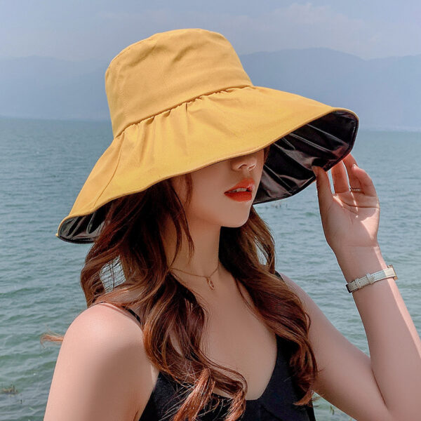 Chapeau anti UV, à large bord, intérieur en vinyle noir, et extérieur de couleur jaune, porté par une mannequin à la plage