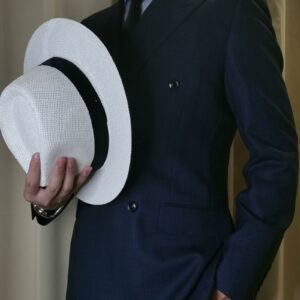 Chapeau panama en paille blanche entouré par un ruban noir, porté dans la main d'un homme en costume