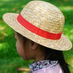 Chapeau en paille beige avec ruban rouge, style Luffy pour enfants, porté par une petite fille de dos