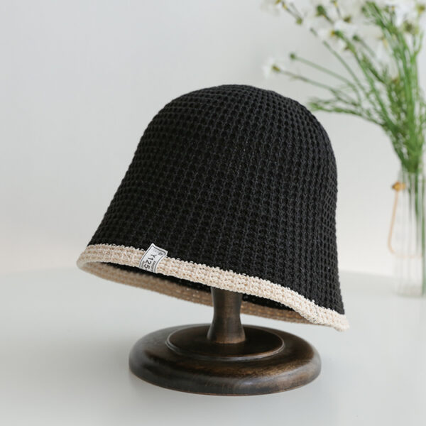 Chapeau cloche respirant de voyage unisexe de couleur noir sur un socle en bois posé sur une table blanche