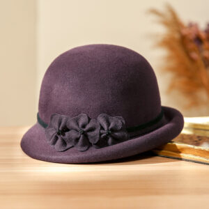 Chapeau cloche en laine avec pompon pour femme de couleur violet posé sur une table en bois