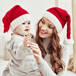 Chapeau de noël à pompons pour enfants et adultes de couleur rouge et blanc, porté par une maman et son bébé dans les bras