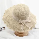Chapeau capeline beige décontracté à bordures sur support en bois lui-même posé sur un tissu blanc.