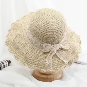 Chapeau capeline beige décontracté à bordures sur support en bois lui-même posé sur un tissu blanc.