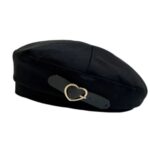 on voit sur un fond blanc un béret noir pour femme avec une boucle en métal en forme de coeur