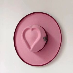 on voit accroché contre un mur un chapeau fedora rose avec un cœur sur le haut pour femme