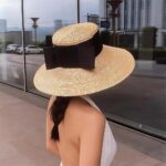 on voit une femme dans la rue avec un chapeau de plage en paille avec un ruban noir pour femme