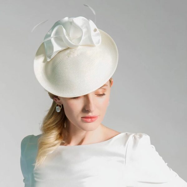 Chapeau bibi de mariage en tissu clair avec nœud plissé et plumes, blanc, porté incliné sur la tête d’une femme en tenue élégante.