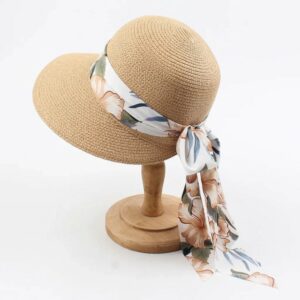 Chapeau de paille beige pour femme avec large foulard à motif floral noué sur le côté, présenté sur un support en bois clair.