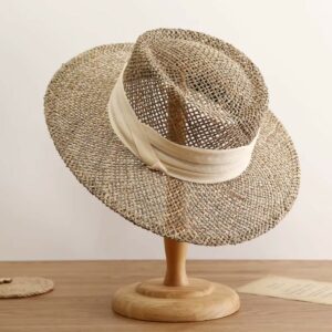 Chapeau style canotier en paille ajourée, avec un ruban beiges sur un support