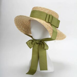 Chapeau romantique en paille avec large ruban vert noué sous le menton, sur une tête de mannequin blanc.