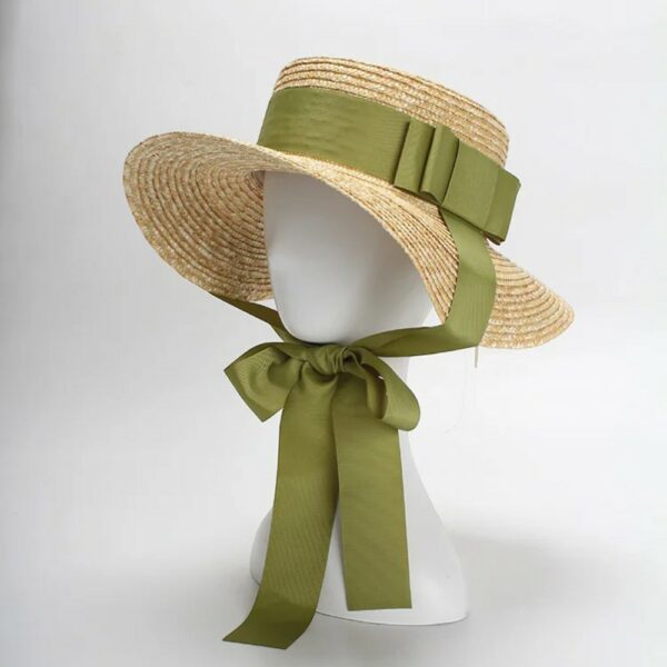 Chapeau romantique en paille avec large ruban vert noué sous le menton, sur une tête de mannequin blanc.