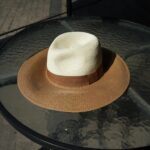 Chapeau bicolore femme chic à large bord, posé sur une table en verre