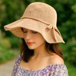 Chapeau capeline anti-UV en maille beige avec nœud décoratif, porté par une femme type européen en extérieur.