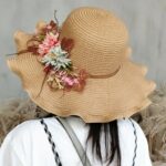 Femme de dos portant un chapeau de paille couleur naturelle, avec des fleurs sur le coté