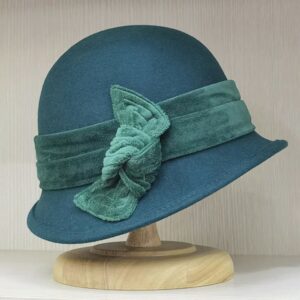 Chapeau cloche femme style années 30 avec nœud décoratif, posé sur un support sur une étagère.